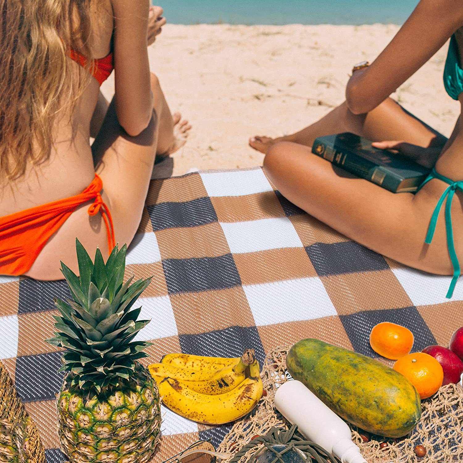 Outdoor ground mat on the beach with fruit and people relaxing